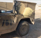 The rear quarter panel of a tan military vehicle, showing significant battle damage from shrapnel.
